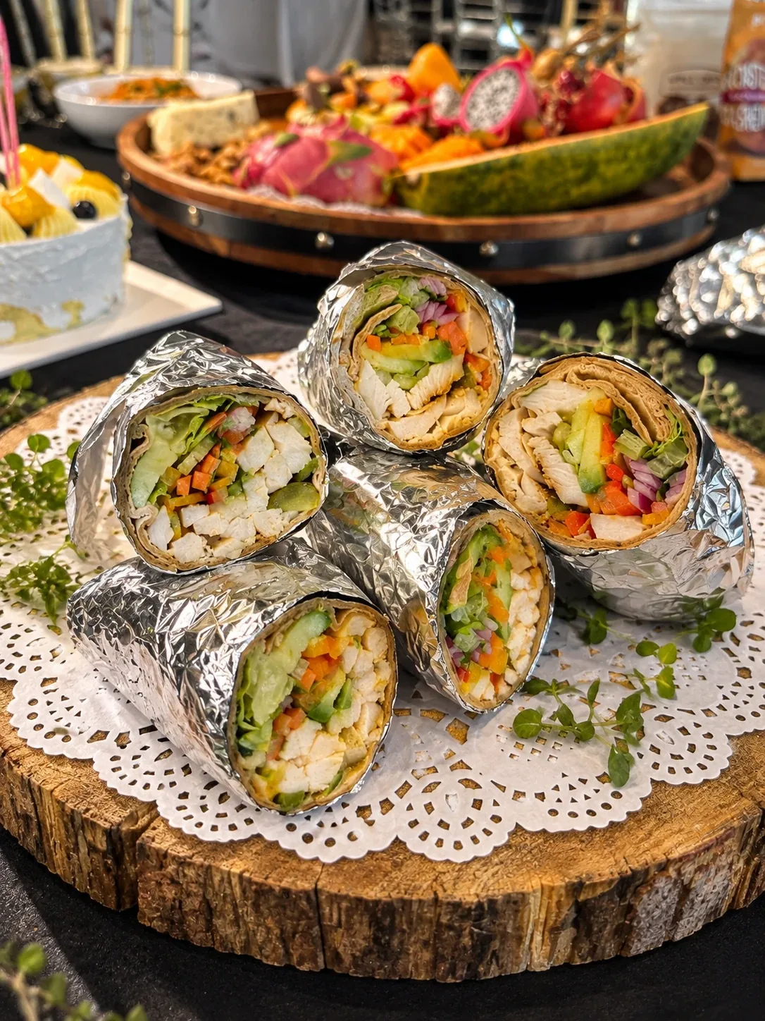Foil-wrapped wraps cut in half and stacked on a wooden board, showing chicken, avocado, peppers and lettuce